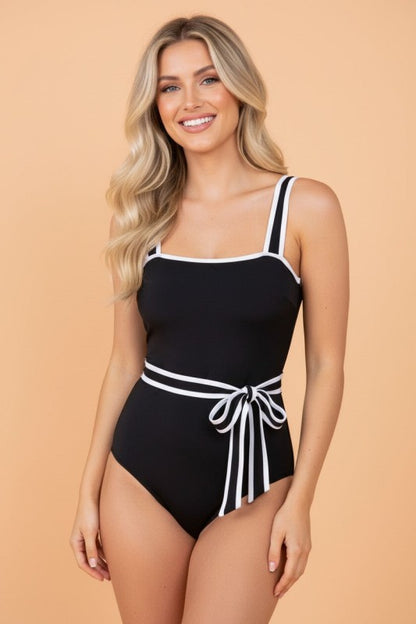 Woman wearing a black and white swimsuit with a tied waist accent.